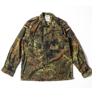 Puede incluir: Camisa de camuflaje en tonos verdes, marrones y negros. La camisa tiene dos bolsillos en el pecho, charreteras y parches de la bandera alemana en las mangas. Una etiqueta es visible cerca del cuello.
