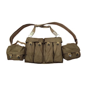 Könnte beinhalten: Olivgrünes militärisches Brustgeschirr mit mehreren Taschen und verstellbaren Riemen. Das Geschirr hat vier Haupttaschen und zwei kleinere Seitentaschen, alle mit Klappenverschlüssen. Die Schultergurte und Verbindungsriemen sind hellbraun.