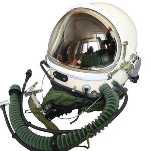 Peut inclure: Casque d'astronaute blanc vintage avec une visière transparente et incurvée. Le casque est équipé d'éléments métalliques et est relié à un tuyau d'oxygène et à un joint de cou verts. L'image est sur fond blanc, soulignant le thème de l'exploration spatiale.