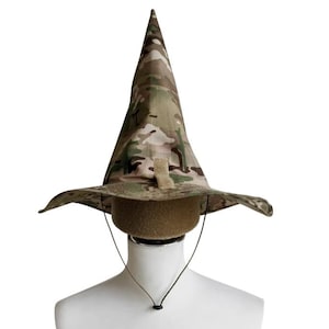 Könnte beinhalten: Ein Tarnmusterhut mit einer hohen, spitzen Krone und einer breiten Krempe. Der Hut wird mit einem Kinnriemen befestigt und wird auf einem Schaufensterkopf präsentiert. Die Farben des Hutes umfassen Grün-, Braun- und Beigetöne.