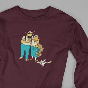 May include: Burgundy long-sleeve shirt featuring a cartoon illustration of two men and a dog. The men are in blue pants and white shirts. The dog is white. The shirt is made of a soft material.