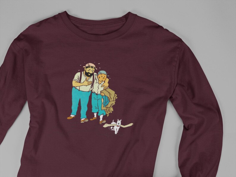 May include: Burgundy long-sleeve shirt featuring a cartoon illustration of two men and a dog. The men are in blue pants and white shirts. The dog is white. The shirt is made of a soft material.