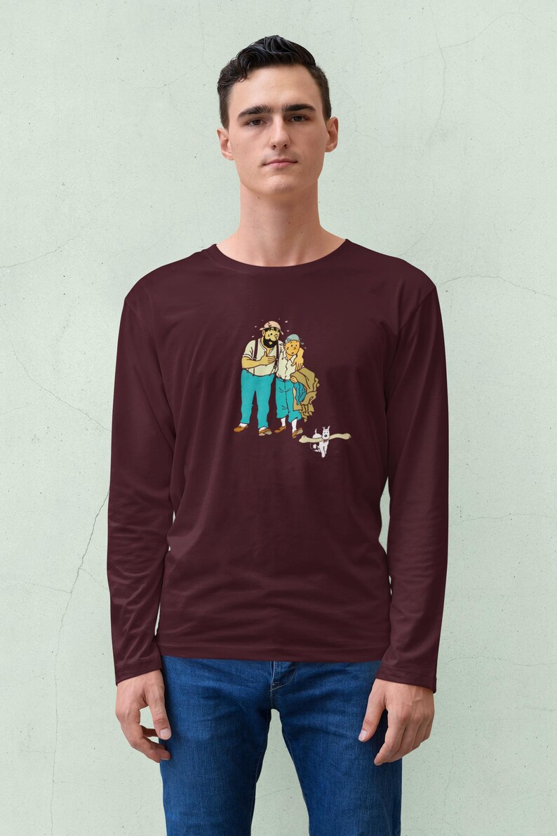 May include: A maroon long-sleeve shirt featuring a cartoon illustration of two people and a cat. The cartoon characters are wearing blue pants and white shirts. The cat is white with black markings. The shirt is made of a soft material.