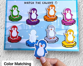 Op de afbeelding: Een kleurenmatching-activiteit met een blauwe achtergrond en geïllustreerde pinguïns op ijsschotsen. De tekst "MATCH THE COLORS" staat bovenaan. Een hand houdt een blauwe pinguïnsticker vast. De tekst "Color Matching Activity" staat onderaan.