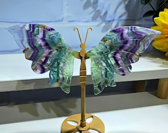 May include: A decorative butterfly sculpture with wings made of translucent, multi-colored fluorite. The wings display shades of purple, green, and blue. The butterfly is mounted on a gold-colored metal stand, creating a unique home decor item.