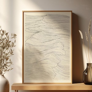 May include: A framed abstract art print with a wave pattern in black lines on a cream backdrop. The artwork is displayed on a wooden bench, with a vase of dried plants and a decorative vase. The style is minimalist and modern, suitable for home decor.