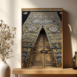 May include: A framed print of the Kaaba door, featuring intricate gold and black detailing. The artwork showcases the door's ornate design, with Arabic calligraphy and geometric patterns. The print is displayed on a wooden bench, with a vase of dried plants on the side.