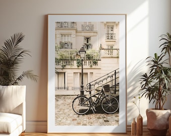 May include: A framed print featuring a Parisian street scene with a black bicycle parked near a lamppost and stairs. The image showcases a classic building with balconies and windows, and is set against a neutral wall with a wooden floor.