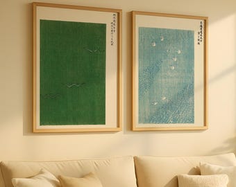 Op de afbeelding: Twee ingelijste prenten met Japanse kunst hangen boven een beige bank. Eén prent heeft een groene achtergrond met vliegende vogels, de andere een blauwe achtergrond met witte vormen. De lijsten zijn van licht hout.