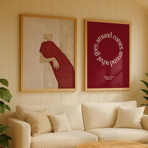 Könnte beinhalten: Ein Wohnzimmer mit cremefarbenem Sofa, beigen Kissen und einem runden Couchtisch aus Holz. An der Wand hängen zwei gerahmte Kunstdrucke, einer zeigt eine Figur in Rot, der andere den Text "What goes around comes around".