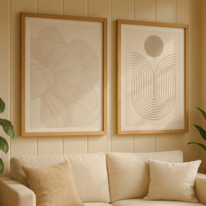 May include: Two framed art prints with light wood frames hang above a cream-colored sofa. One print features a floral design in shades of beige, while the other showcases an abstract geometric pattern with a circular element. A woven pillow and a solid pillow rest on the sofa.