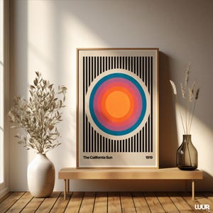 May include: A framed art print featuring a retro design of concentric circles in orange, pink, blue, and white, set against a black and white striped background. The text "The California Sun" and the year "1919" are printed at the bottom.