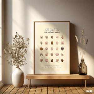 Puede incluir: Una impresión enmarcada con el texto "all butts are welcome here!" e ilustraciones de varias nalgas. La impresión se muestra en un banco de madera con un jarrón de flores secas y un jarrón decorativo.