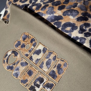 May include: Close-up of a khaki-colored fabric with the embroidered words "Girl Power" in a leopard print design. A leopard print fabric is visible in the background.