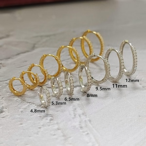 May include: An assortment of hoop earrings in gold and silver tones, ranging in size from 4.8mm to 12mm. The earrings are adorned with small, sparkling stones, creating a delicate and elegant appearance. The image showcases various sizes for comparison.