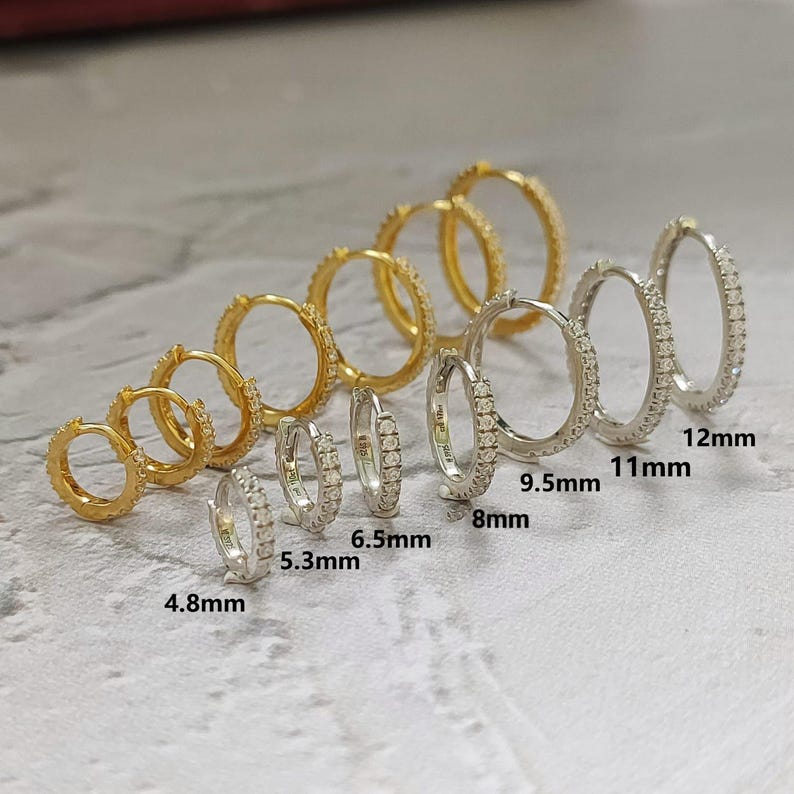 May include: An assortment of hoop earrings in gold and silver tones, ranging in size from 4.8mm to 12mm. The earrings are adorned with small, sparkling stones, creating a delicate and elegant appearance. The image showcases various sizes for comparison.
