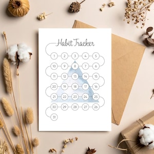 May include: A white habit tracker with the title "Habit Tracker" in a cursive font. The tracker features a series of numbered circles, arranged in a zig-zag pattern, with a light blue triangle in the center. The design is simple and minimalist.