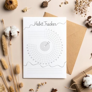 May include: A white habit tracker with the words "Habit Tracker" at the top. The tracker features a circular design with numbers and a target graphic in the center. The background is a neutral beige.