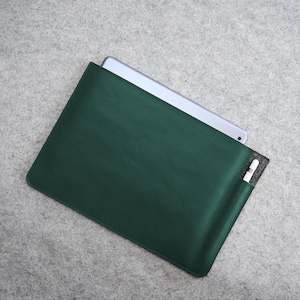 May include: A dark green leather tablet sleeve with a silver tablet partially inserted. A white stylus is in a small pocket on the side. The sleeve is rectangular and has a stitched border.