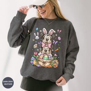 Puede incluir: Sudadera gris oscuro jaspeada con un gr&aacute;fico colorido de Pascua. El dise&ntilde;o incluye a Mickey y Minnie Mouse disfrazados de conejos, rodeados de huevos de Pascua, zanahorias y flores. La sudadera tiene cuello redondo y mangas largas.