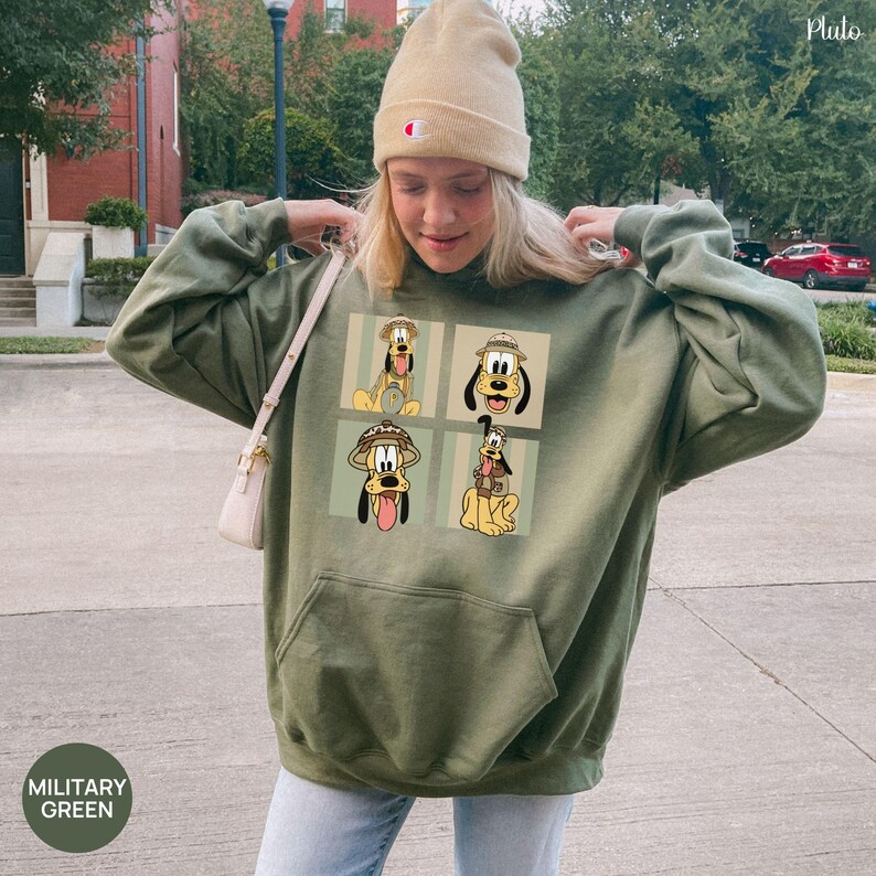May include: Military green hoodie featuring a four-panel graphic of Pluto in various safari-themed poses. The hoodie has a kangaroo pocket and a drawstring hood. The text "MILITARY GREEN" is in a circle at the bottom left.