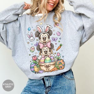 Puede incluir: Sudadera gris deportiva con un dise&ntilde;o colorido de Pascua. El dise&ntilde;o incluye a Mickey y Minnie Mouse disfrazados de conejos, huevos de Pascua, zanahorias y flores. La sudadera tiene cuello redondo y mangas largas.