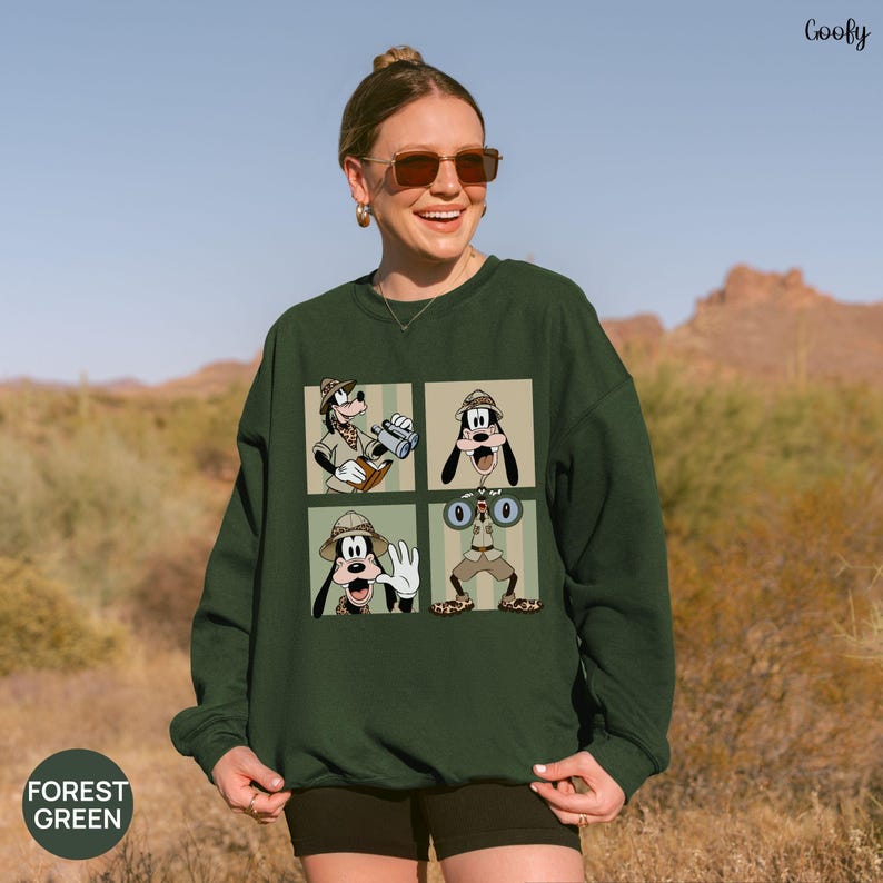 May include: Forest green sweatshirt featuring a four-panel graphic of Goofy in safari attire. Each panel shows Goofy in a different pose, with binoculars, a camera, and a waving gesture. The word "Coofy" is in the top right corner.