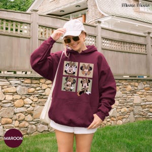 May include: Maroon hoodie featuring a four-panel design of Minnie Mouse in various poses with leopard print accents. The hoodie has a kangaroo pocket and a drawstring hood. The word "MAROON" is printed on a maroon circle at the bottom left.