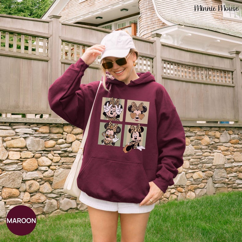 May include: Maroon hoodie featuring a four-panel design of Minnie Mouse in various poses with leopard print accents. The hoodie has a kangaroo pocket and a drawstring hood. The word "MAROON" is printed on a maroon circle at the bottom left.