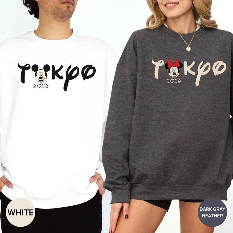 May include: White and dark gray heather sweatshirts with the word "Tokyo" in a script font, featuring a Mickey Mouse graphic and the year "2026". The white sweatshirt has black text, while the dark gray one has beige text and a Minnie Mouse graphic.