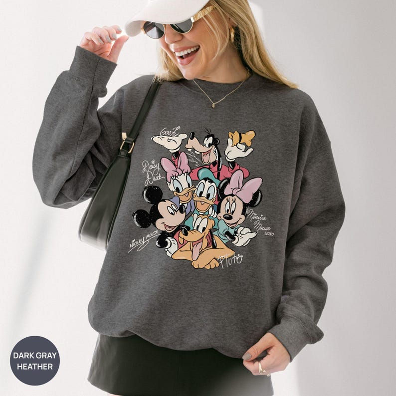 K&ouml;nnte beinhalten: Dunkelgraues Heather-Sweatshirt mit einem farbenfrohen Aufdruck von Disney-Figuren wie Micky Maus, Minnie Maus, Donald Duck und Goofy. Das Sweatshirt hat einen Rundhalsausschnitt und lange &Auml;rmel. Der Text "Dark Gray Heather" befindet sich unten links.