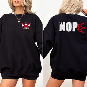 May include: Black sweatshirt with a white crew neck collar. The front features a red and white crown graphic. The back of the sweatshirt displays the word "NOPE" in white block letters with a red crown graphic.