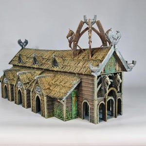 Könnte beinhalten: Ein detailliertes Miniaturmodell eines Wikinger-Langhauses. Das Gebäude verfügt über ein Strohdach, Holzwände und dekorative Schnitzereien. Das Modell umfasst architektonische Details wie Dachfenster, gewölbte Türen und Zierdachaufsätze. Die Farbpalette umfasst Braun-, Beige- und Grüntöne.