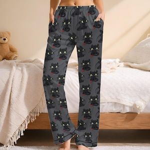May include: Gray pajama pants with a repeating pattern of black cartoon dragons with red tongues and yellow eyes. The pants have a relaxed fit with pockets and a drawstring waist. The pajama pants are made of a soft, comfortable material.