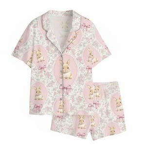 Puede incluir: Un conjunto de pijama de dos piezas con un patr&oacute;n repetido de conejitos en &oacute;valos rosas con lazos rosas sobre un fondo blanco con acentos florales rosas. El conjunto incluye una camisa con botones y mangas cortas y pantalones cortos a juego.