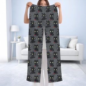 May include: Gray pajama pants with a repeating pattern of a cartoon dragon character. The dragon is black with yellow eyes and a red tongue. The pants are held up in front of a person.