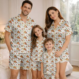 May include: Matching family pajama sets featuring a white background with a repeating pizza slice pattern. The sets include short-sleeved button-up shirts and matching shorts, trimmed with yellow piping. The family of four is wearing the pajamas.