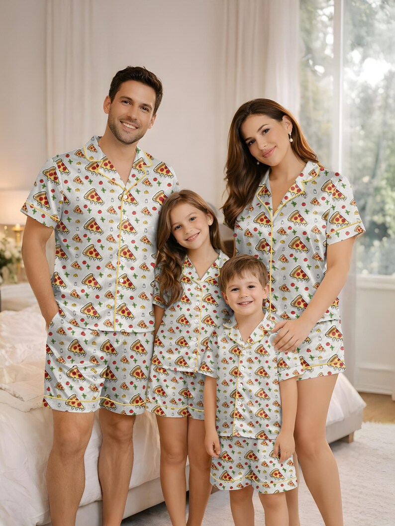 May include: Matching family pajama sets featuring a white background with a repeating pizza slice pattern. The sets include short-sleeved button-up shirts and matching shorts, trimmed with yellow piping. The family of four is wearing the pajamas.