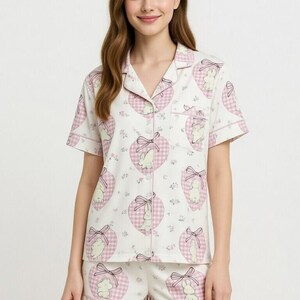 May include: White pajama set with a pink heart and bunny print. The short-sleeved top and shorts feature a button-down design and pink trim. The word "PAJAMA" is written in pink at the top.