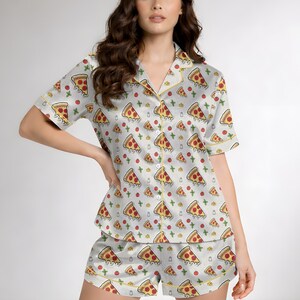 May include: A light gray pajama set featuring a pizza slice pattern. The short-sleeved top and shorts are adorned with repeating illustrations of pizza slices, tomatoes, and cheese. The set has yellow trim.