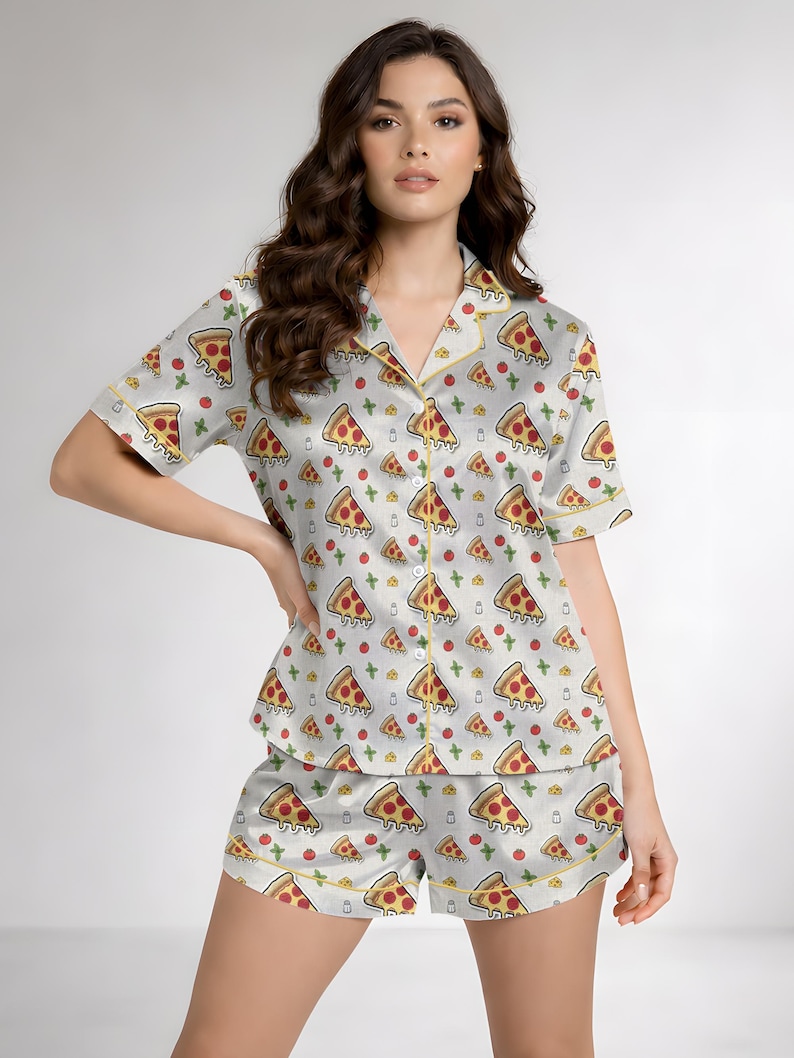 May include: A light gray pajama set featuring a pizza slice pattern. The short-sleeved top and shorts are adorned with repeating illustrations of pizza slices, tomatoes, and cheese. The set has yellow trim.