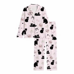 May include: Pale pink pyjama set with a black cat pattern. The set includes a button-down top and matching trousers. The design features black cat illustrations, hearts, and the word "Love".