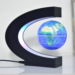 Peut inclure: Un globe terrestre en lévitation avec une carte du monde détaillée, suspendu dans un cadre noir en forme de C. Le cadre est éclairé par une lumière LED. Le globe est bleu avec des continents verts et jaunes.