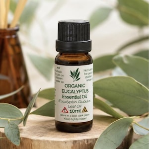 May include: A small amber glass bottle of organic eucalyptus essential oil with a black cap. The white label features green text reading Organic Eucalyptus Essential Oil, Eucalyptus Globulus Leaf Oil, and 10ml, along with two yellow warning triangles.