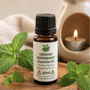 May include: A small amber glass bottle of organic peppermint essential oil with a black cap. The white label features green text reading Organic Peppermint Essential Oil, Mentha Piperita, and 10ml, along with two yellow warning triangle icons.