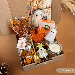 Könnte beinhalten: Eine Pappschachtel mit einem Halloween-Geschenkset: ein durchsichtiger Beutel mit Kürbis-Motiv und Boo-Yah-Anhänger, ein kleiner orangefarbener Stoffkürbis, eine weiße Geisterfigur, ein Glas Honig, ein goldener Löffel und ein Kürbisgewürz-Teebeutel.