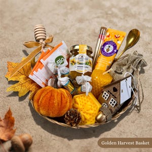 Könnte beinhalten: Ein geflochtener Korb mit einem Glas Breitsamer Sonnenblumenhonig, einer Tube Honig-Handcreme, einem hölzernen Honiglöffel mit goldenem Band, einem kleinen orangefarbenen Samtkürbis, einer wabenförmigen Wachskerze, einem Holzhaus-Ornament und Teebeuteln.