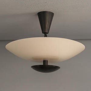May include: A modern ceiling light fixture with a white, bowl-shaped shade and a dark bronze-colored stem and base. The light is mounted on a gray ceiling, showcasing a minimalist design.