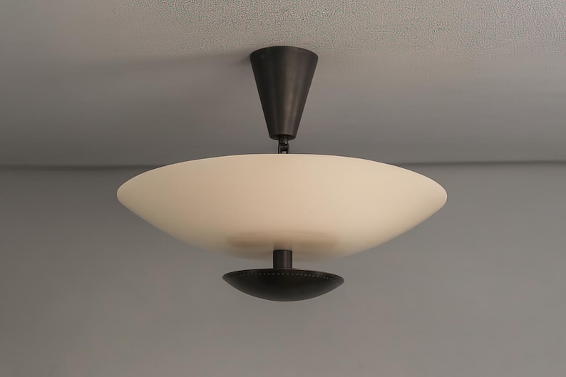 May include: A modern ceiling light fixture with a white, bowl-shaped shade and a dark bronze-colored stem and base. The light is mounted on a gray ceiling, showcasing a minimalist design.