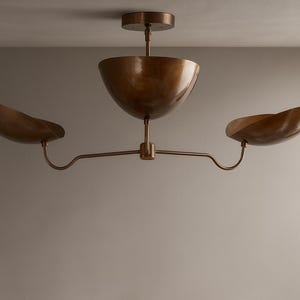 May include: A bronze ceiling light fitting with three bowl-shaped shades. The central shade is larger, with two smaller shades extending outwards. The fitting is mounted on a ceiling plate.
